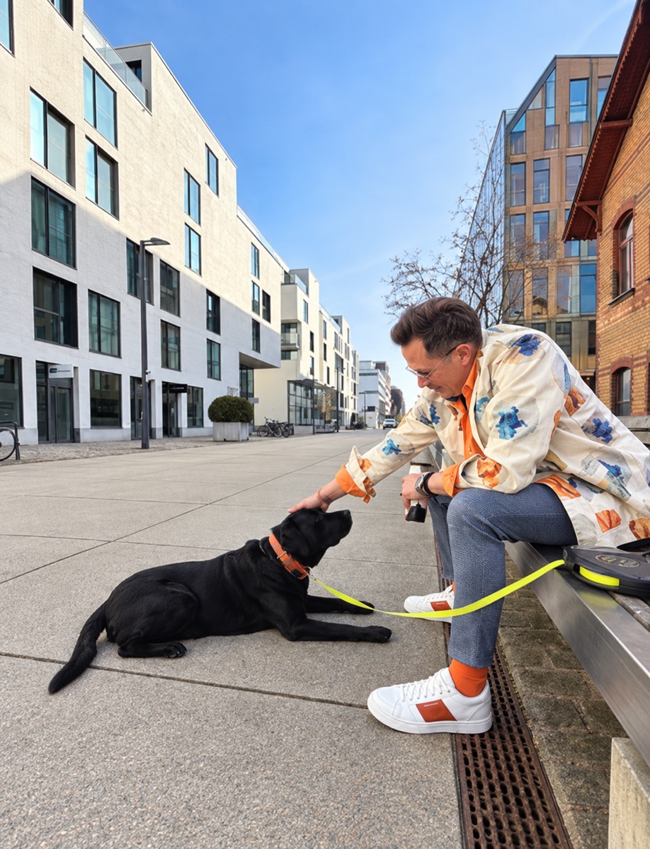 Jan Eric Bollig sitzt auf einer Bank in der Stadt und streichelt seinen schwarzen Hund Buddy